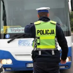 Policjant w kamizelce odblaskowej kieruje ruchem przy autokarze turystycznym. Ciekawe, ile zarabiają ochroniarze w porównaniu do jego pensji.