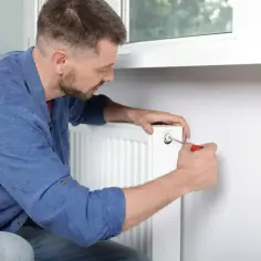 Mężczyzna reguluje odpowietrznik grzejnika, próbując rozwiązać problem, dlaczego grzejnik jest zimny na dole.