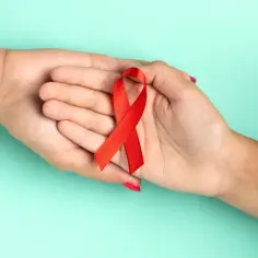 Dwie dłonie trzymające czerwoną wstążkę symbolizującą walkę z aids. Wsparcie i nadzieja.