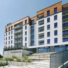 Nowe inwestycje Gdynia: nowoczesny budynek mieszkalny z drewnianymi elementami i przeszklonymi balkonami.