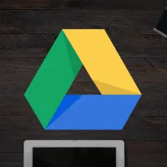 Logo Google Drive na drewnianym tle. Obok leżą aparat, portfel, okulary i smartfon. To idealne miejsce na kopia zapasowa google.