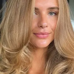 Kobieta z pięknymi, falowanymi włosami w odcieniu maślany blond. Jej zielone oczy i delikatny uśmiech dodają jej uroku.