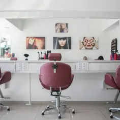 Wnętrze salonu fryzjerskiego. Trzy różowe fotele fryzjerskie przed lustrem, na ścianie obrazy z modelkami. To idealny lokal użytkowy dla stylistów.