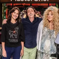 Trzech jurorów MasterChef: uśmiechnięta kobieta w koszulce z bykiem, mężczyzna w granatowej koszuli i kobieta z burzą blond loków.