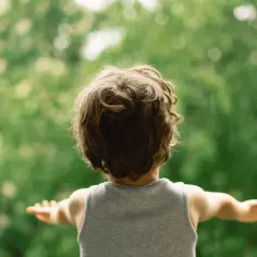 Dziecko z rozłożonymi rękami na tle zieleni. Kwasy omega-3 dla dzieci nadpobudliwych mogą pomóc w uspokojeniu.