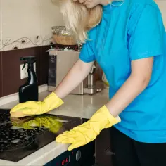 Kobieta w żółtych rękawiczkach czyści płytę ceramiczną, aby usunąć zapach spalonego mleka z płyty ceramicznej bez rysowania szkła.