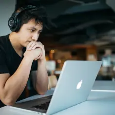 Młody mężczyzna w słuchawkach analizuje informacje na laptopie, szukając odpowiedzi na pytanie, jak sprawdzić wyniki egzaminów zawodowych.