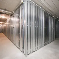 Korytarz z rzędami metalowych komórek lokatorskich. Widać instalacje biegnące pod sufitem.