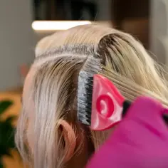 Profesjonalna dekoloryzacja włosów w salonie. Różowa rękawiczka i pędzel do nakładania rozjaśniacza na blond pasma.