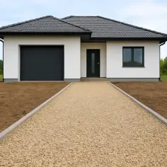 Nowy dom z garażem i drzwiami, przed którym rozciąga się podjazd z kruszywa.