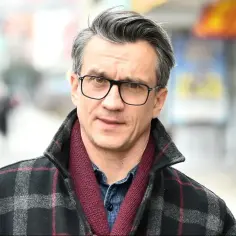 Michał Czernecki w okularach i płaszczu w kratę, gotowy do kolejnych filmów, seriali i programów.