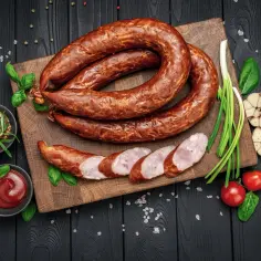 Aromatyczne wędzenie kiełbasy swojskiej na drewnianej desce. Obok czosnek, pomidorki, szczypiorek i musztarda.