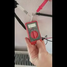 Jak sprawdzić kabel antenowy miernikiem? Ręka trzyma czerwony miernik, sondy dotykają odsłoniętych przewodów kabla.