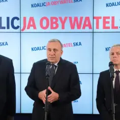 Trzech mężczyzn w garniturach przemawia na tle ekranów z napisem "Koalicja Obywatelska". Ich program polityczny jest kluczowy.