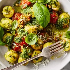 Pyszne gnocchi z pesto, pomidorkami i orzeszkami pinii, udekorowane świeżą bazylią. Idealne danie dla miłośników włoskich smaków.