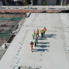 Grupa budowlańców na placu budowy. Widać zbrojenie i świeży beton. Sprawdzają beton b25 cena za m3.