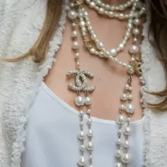 Elegancki biały żakiet, pod nim biała bluzka, a na szyi kaskada pereł i naszyjniki z logo Chanel.
