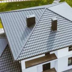 Widok z góry na szary dach czterospadowy z dwoma kominami i zielonym ogrodem.