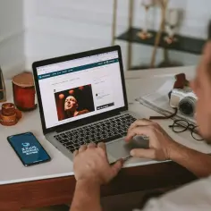 Mężczyzna pracuje na laptopie, szukając informacji, jak sprawdzić model laptopa. Na biurku leży też telefon z aplikacją "Życie ciekawsze niż historie".