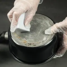 Ręce w rękawiczkach czyszczą przypalony spód garnka gąbką. Czy pasta z sody i octu naprawdę działa na przypalony spód garnka?