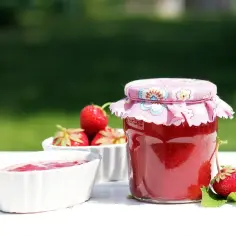 Słoik z domowym dżemem truskawkowym, miseczka z dżemem i świeże truskawki.