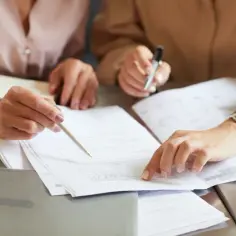 Dwie kobiety analizują dokumenty, szukając informacji o tym, co wpisać w umowie z oddziałem NFZ.