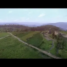Krajobraz z gry Kingdom Come: Deliverance. Wiatrak i domy na wzgórzu, pola uprawne i lasy w tle. Czas gry to piękny, otwarty świat.