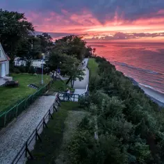 Zachód słońca nad morzem w Jastrzębiej Górze. Spacerowicze na klifie, domki i piękne, różowe niebo.