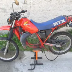 Pomarańczowy motocykl Honda MTX 125 z niebieskim siedzeniem, gotowy do jazdy po wertepach.