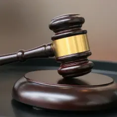 Młotek sędziowski z drewnianą rękojeścią i złotym pierścieniem na drewnianej podstawie.