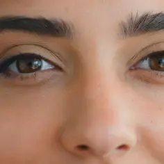 Brązowe oczy z subtelnym makijażem podkreślającym ich kształt, nadając spojrzeniu charakterystyczne foxy eyes.