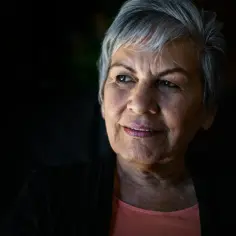 Portret starszej kobiety z siwymi włosami, która patrzy w bok z delikatnym uśmiechem. Jej oczy zdają się opowiadać historię o tym, na co umierają chorzy na Alzheimera – o utracie wspomnień.