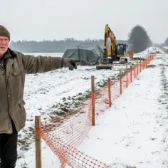 Mężczyzna wskazuje na teren budowy drogi, pytając, czy gmina może zabrać część działki. W tle koparka i pracownicy.