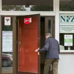 Starszy pan wchodzi do przychodni NFZ. Może tam uzyskać informacje o świadczeniach, np. 500 plus dla chorych na raka zus.