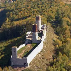 Ruiny zamku Chęciny na wzgórzu, otoczone jesiennym lasem. Sprawdź zamek Chęciny cennik biletów i zaplanuj wizytę!