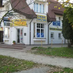 Budynek z żółtymi szyldami "OKNA DRZWI" i "DRZWI PARAPETY".