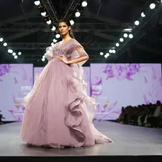 Modelka prezentuje suknię haute couture w kolorze pudrowego różu z falbanami i zdobieniami na wybiegu.