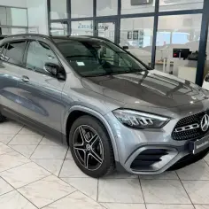 Szary Mercedes GLA 200 z czarnymi felgami stoi w salonie obok białego Mercedesa.