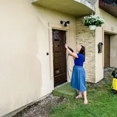 Kobieta myje elewację domu myjką ciśnieniową. Uważaj, czy myjka ciśnieniowa może zniszczyć elewację domu przy złym ciśnieniu.