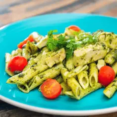 Penne z kurczakiem i sosem pesto, ozdobione pomidorkami koktajlowymi i natką pietruszki. Pyszny makaron z mozzarellą w tle.