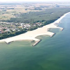 Polski Dubaj nad morzem: malownicza plaża z falochronami, las i zabudowania kurortu.