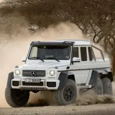 Biały Mercedes 6x6 szaleje po pustyni, wzbijając tumany kurzu.