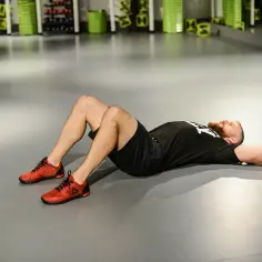 Mężczyzna w czerwonych butach wykonuje ćwiczenia na oponkę na brzuchu, leżąc na plecach z ugiętymi nogami.