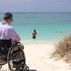 Mężczyzna z tetraplegią w wózku inwalidzkim podziwia piękny widok na turkusowe morze i plażę.