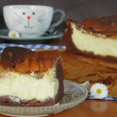 Pyszne izaura ciasto, kawałek na talerzyku, obok cały sernik i filiżanka z kotkiem.