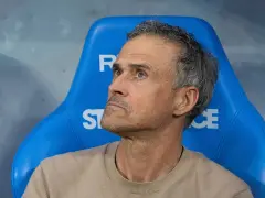 Luis Enrique, kto jest trenerem PSG, siedzi na niebieskiej ławce, zamyślony.