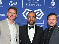 Trzech mężczyzn na tle PKO Bank Polski Ekstraklasa. Jeden z nich, w garniturze, uśmiecha się do obiektywu, być może jako jeden z przyszłych królowie strzelców ekstraklasy.
