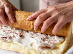 Ręce zwijają biszkopt z kremem i truskawkami. To najprostsza rolada biszkoptowa, która zachwyci smakiem.