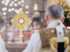 Goldene Monstranz mit Hostie im Schein von Kerzenlicht. Ein Priester in festlicher Kleidung feiert die Messe, ein Moment des weihnachtlichen Christentums.