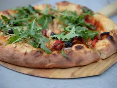 Idealne ciasto na pizzę z rukolą, oliwkami i papryką, wypieczone na drewnianej desce.